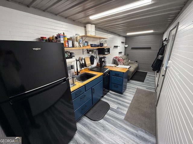 kitchen featuring blue cabinetry, butcher block counters, light wood-style flooring, a sink, and black appliances