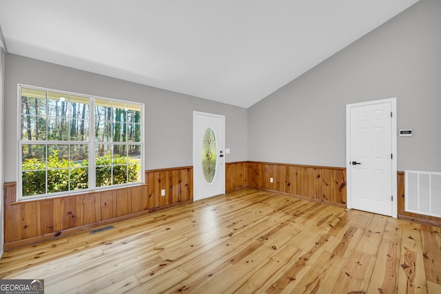 empty room featuring lofted ceiling, wainscoting, wood-type flooring, and visible vents