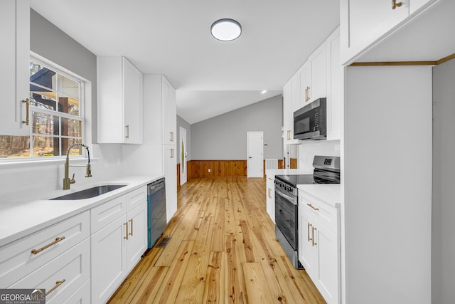 kitchen with white cabinets, wainscoting, vaulted ceiling, stainless steel appliances, and a sink