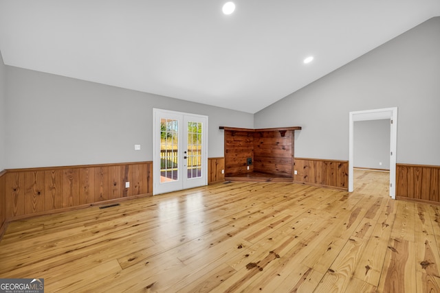 unfurnished living room featuring lofted ceiling, a wainscoted wall, hardwood / wood-style floors, and french doors