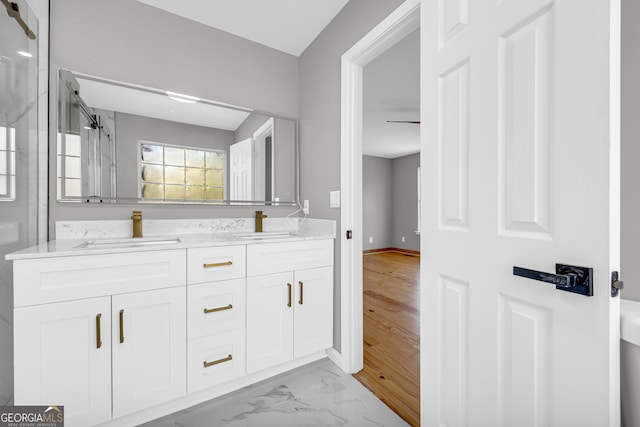 bathroom with marble finish floor, a marble finish shower, double vanity, a sink, and baseboards
