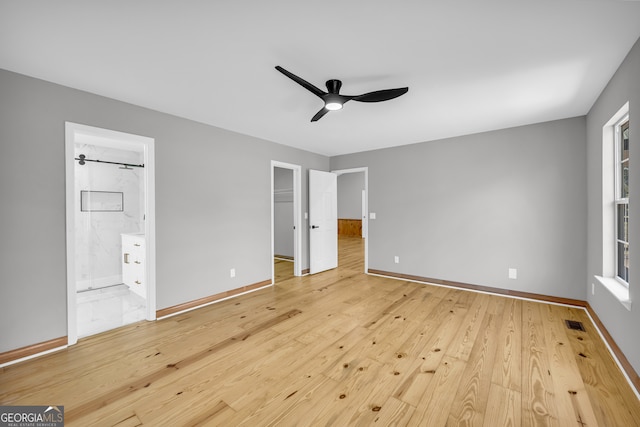unfurnished bedroom featuring a walk in closet, visible vents, light wood-style flooring, and baseboards