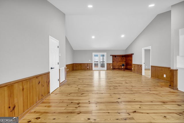 unfurnished living room featuring french doors, wainscoting, vaulted ceiling, and light wood-style flooring