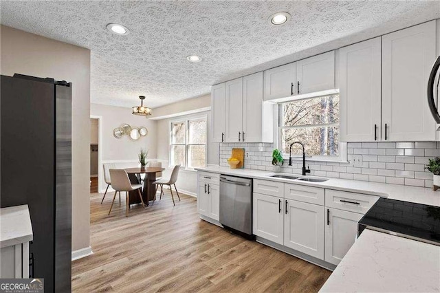 kitchen featuring a sink, white cabinetry, appliances with stainless steel finishes, light wood finished floors, and tasteful backsplash