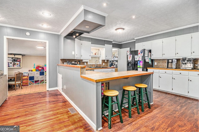 kitchen with black fridge with ice dispenser, wood finished floors, a textured ceiling, ornamental molding, and a sink