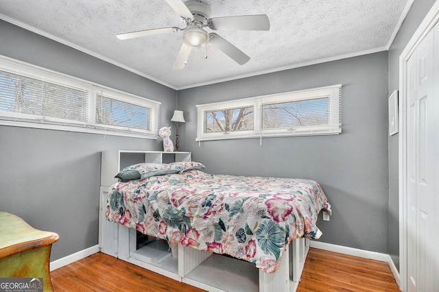 bedroom featuring wood finished floors, a closet, baseboards, a ceiling fan, and ornamental molding