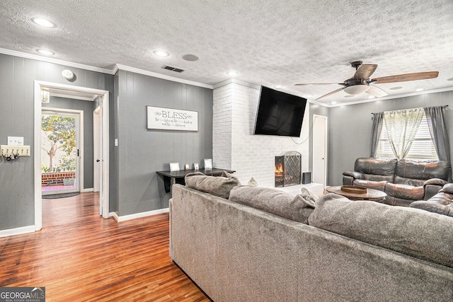 living area with ornamental molding, wood finished floors, a textured ceiling, a fireplace, and ceiling fan