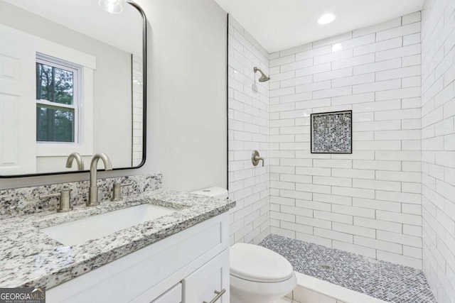 full bathroom featuring a tile shower, vanity, and toilet