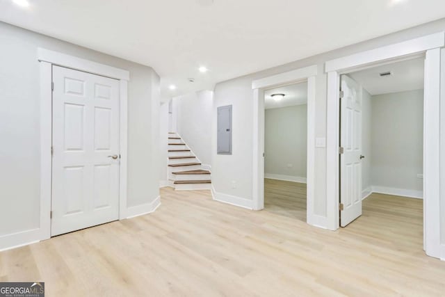 below grade area with baseboards, electric panel, light wood finished floors, and stairs