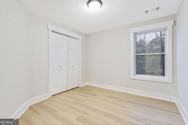 unfurnished bedroom featuring light wood finished floors, visible vents, baseboards, and a closet