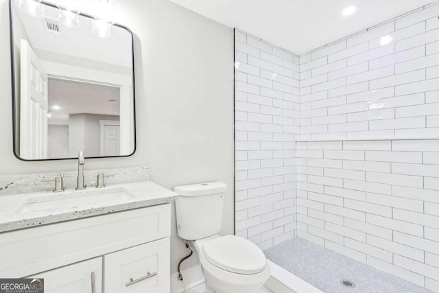 bathroom with visible vents, tiled shower, vanity, and toilet