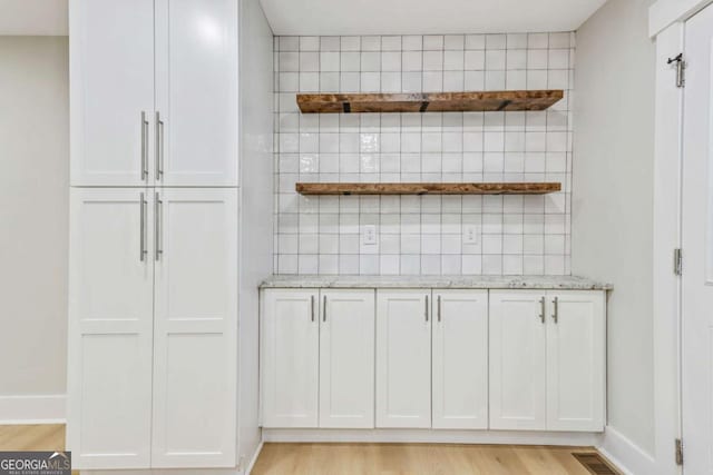 kitchen with white cabinets, light stone countertops, light wood-style flooring, and open shelves