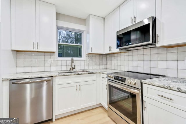 kitchen featuring stainless steel appliances, white cabinets, a sink, and decorative backsplash