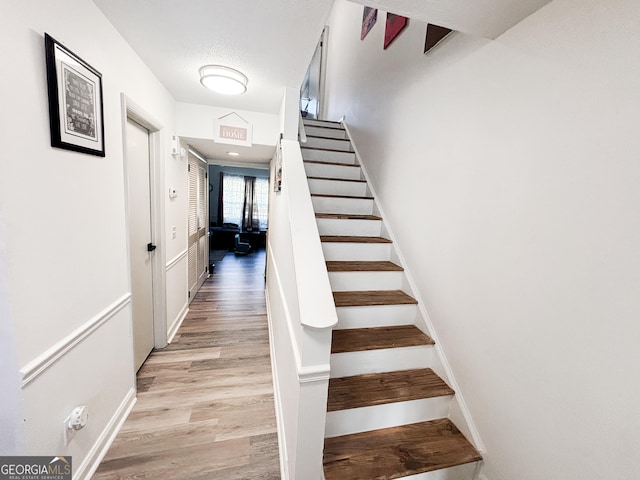 staircase with a textured ceiling, wood finished floors, and baseboards