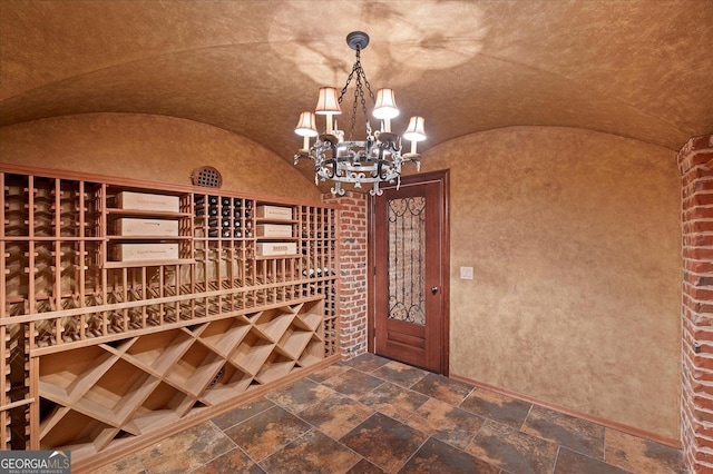 wine area with lofted ceiling, stone tile floors, and an inviting chandelier