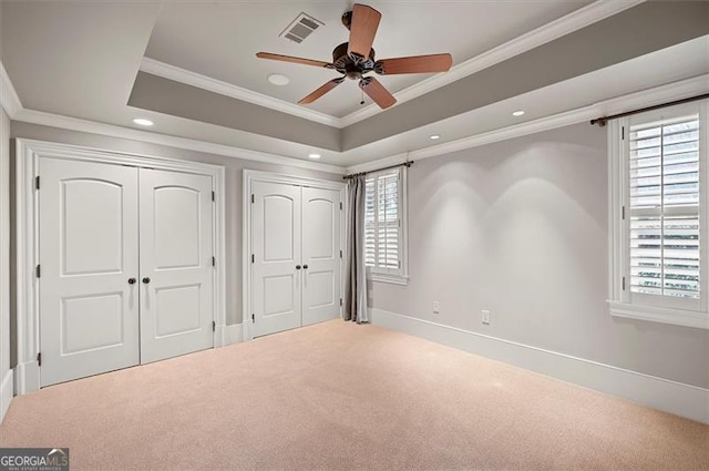 unfurnished bedroom with two closets, multiple windows, carpet floors, ornamental molding, and baseboards