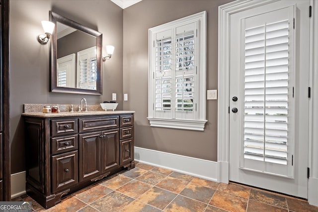 bathroom with stone tile floors, vanity, and baseboards