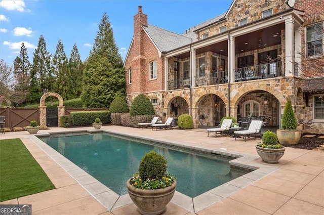 back of house with stone siding, a balcony, a patio area, and an outdoor pool