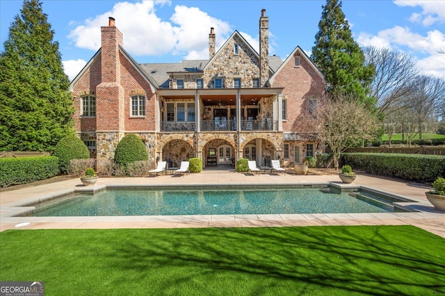 back of house featuring a balcony, stone siding, a lawn, and a patio