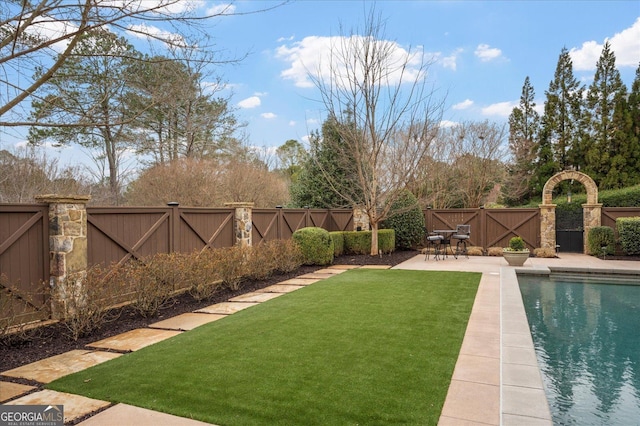 view of yard featuring a fenced in pool, a patio area, a fenced backyard, and a gate