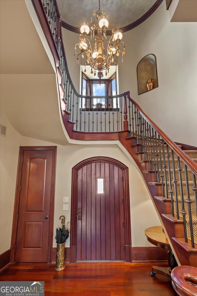 entryway with an inviting chandelier, crown molding, a high ceiling, and wood finished floors