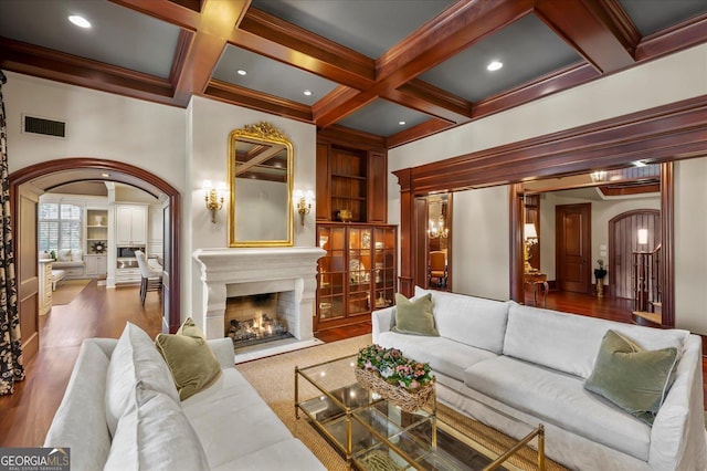 living room with built in features, arched walkways, beam ceiling, visible vents, and wood finished floors