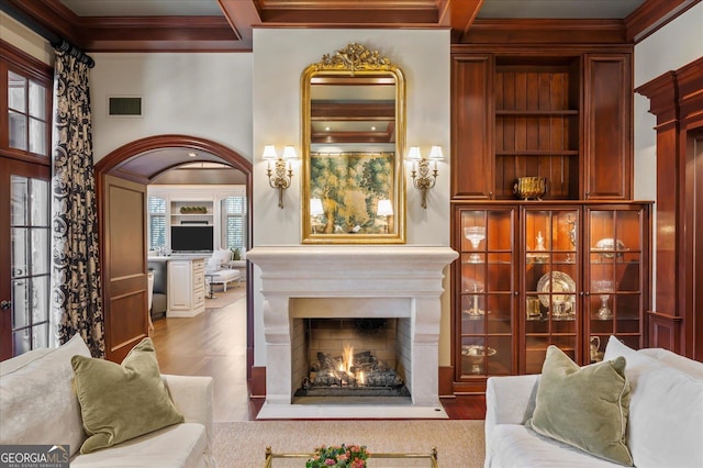 living area with a warm lit fireplace, ornamental molding, beamed ceiling, and visible vents