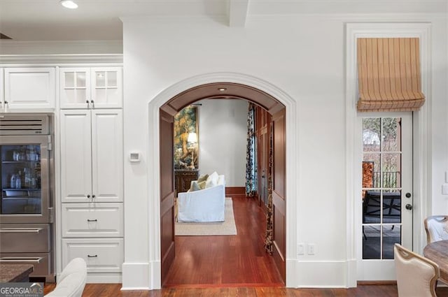 hallway with arched walkways, wood finished floors, baseboards, ornamental molding, and recessed lighting