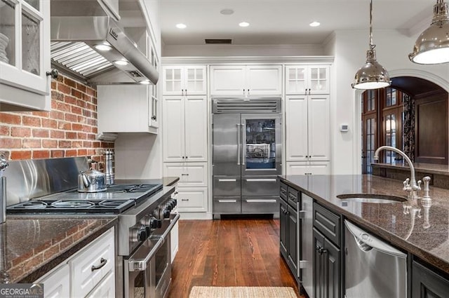 kitchen with high end appliances, exhaust hood, a sink, white cabinets, and crown molding
