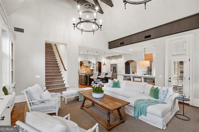 living area with high vaulted ceiling, stairway, a chandelier, and baseboards