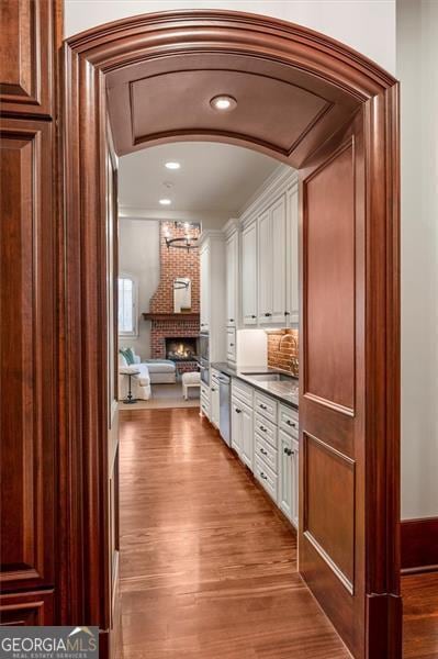 bar area featuring stainless steel dishwasher, a sink, wood finished floors, a fireplace, and arched walkways