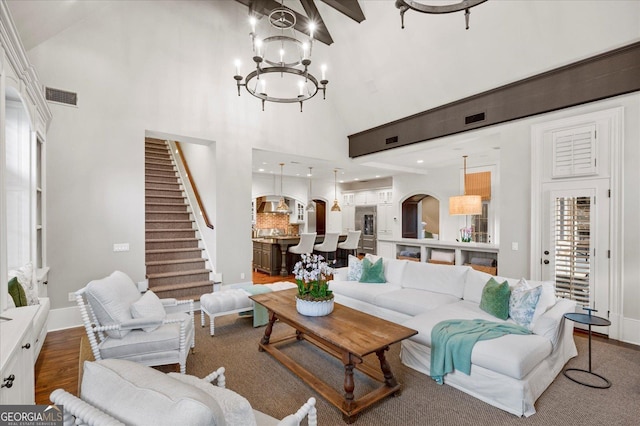 living room featuring high vaulted ceiling, a notable chandelier, wood finished floors, visible vents, and stairway