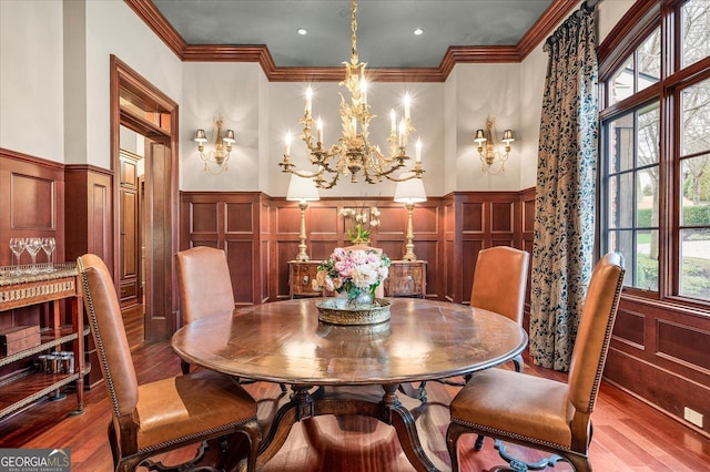 dining room with wainscoting, wood finished floors, an inviting chandelier, crown molding, and a decorative wall