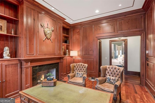 sitting room with a fireplace, built in shelves, wood finished floors, and crown molding