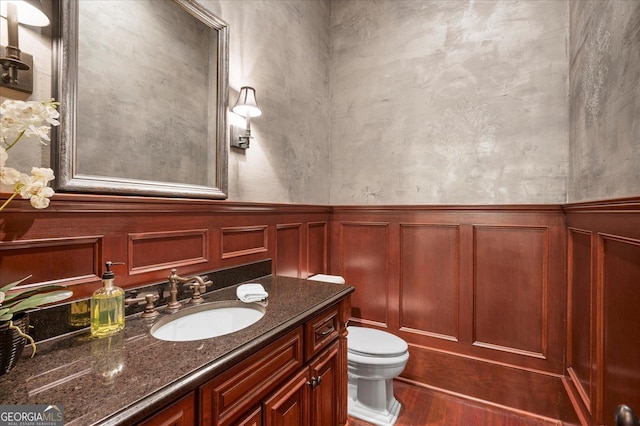 bathroom with wood finished floors, wainscoting, vanity, and toilet