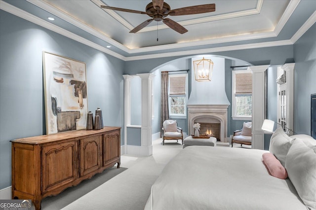 bedroom with arched walkways, decorative columns, a raised ceiling, light carpet, and a lit fireplace