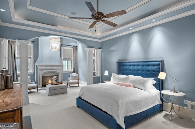 bedroom with arched walkways, a fireplace, decorative columns, a raised ceiling, and carpet flooring