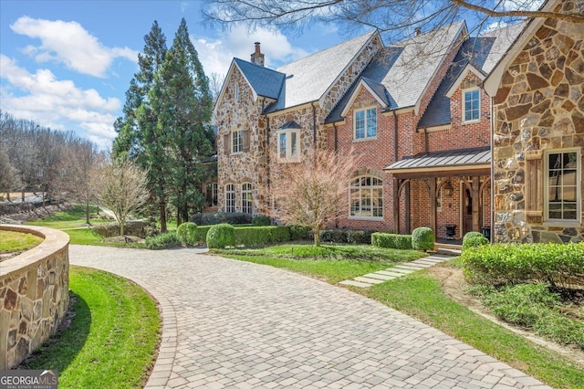 english style home featuring brick siding, a chimney, a standing seam roof, a high end roof, and stone siding