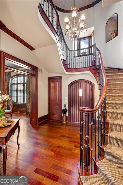 foyer featuring stairs, wood finished floors, crown molding, a chandelier, and arched walkways