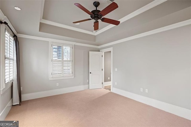 unfurnished bedroom featuring carpet, a tray ceiling, crown molding, baseboards, and a ceiling fan