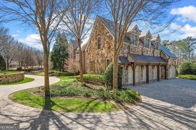 view of side of home with a garage, stone siding, a standing seam roof, and driveway