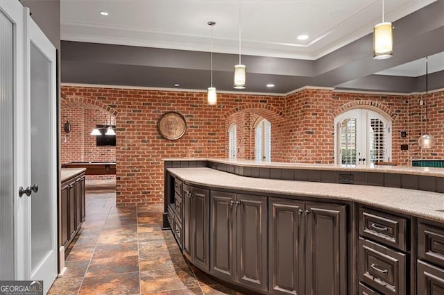 kitchen featuring brick wall, crown molding, dark stone finish floors, pendant lighting, and light countertops