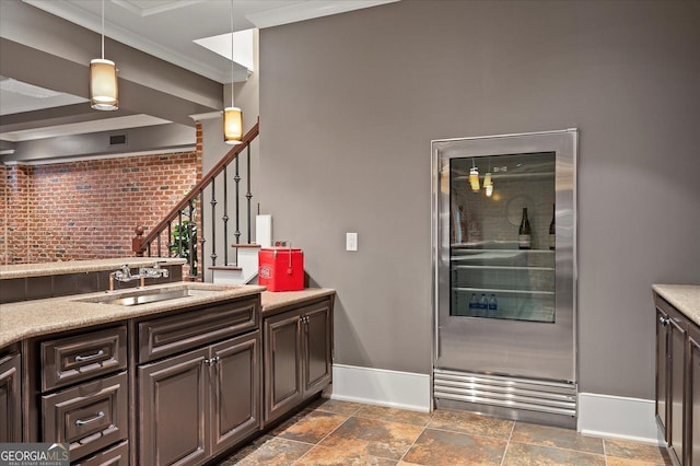 kitchen with stone tile floors, baseboards, crown molding, pendant lighting, and a sink