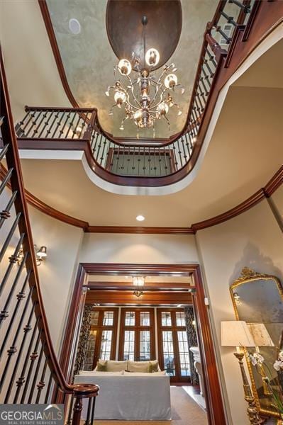 foyer with a towering ceiling, ornamental molding, french doors, and a chandelier