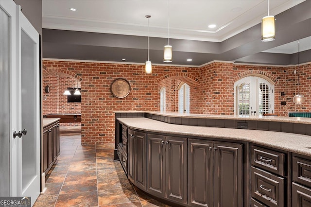 kitchen featuring pendant lighting, crown molding, stone tile floors, light countertops, and brick wall