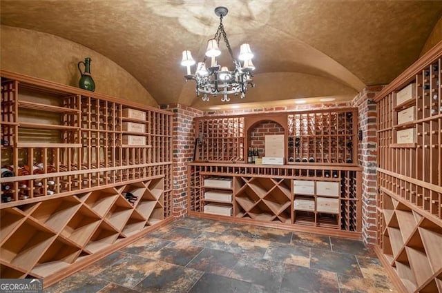 wine room with vaulted ceiling, stone finish floors, and a chandelier