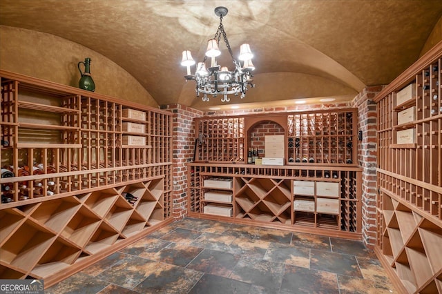 wine area with vaulted ceiling, stone finish flooring, and a notable chandelier