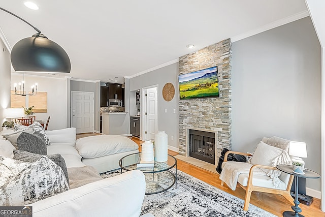 living area featuring baseboards, crown molding, light wood-style floors, a fireplace, and a notable chandelier