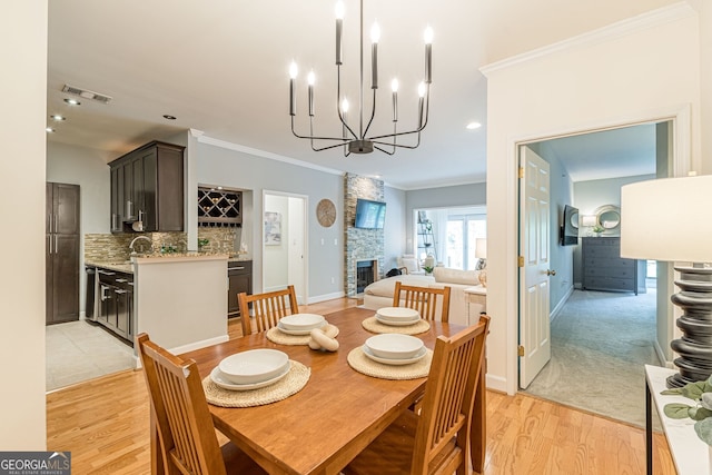 dining area featuring visible vents, crown molding, a stone fireplace, light wood-style floors, and a notable chandelier