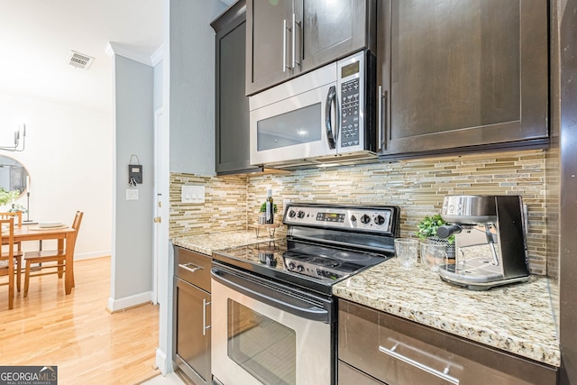 kitchen with stainless steel appliances, visible vents, decorative backsplash, light wood-style floors, and light stone countertops